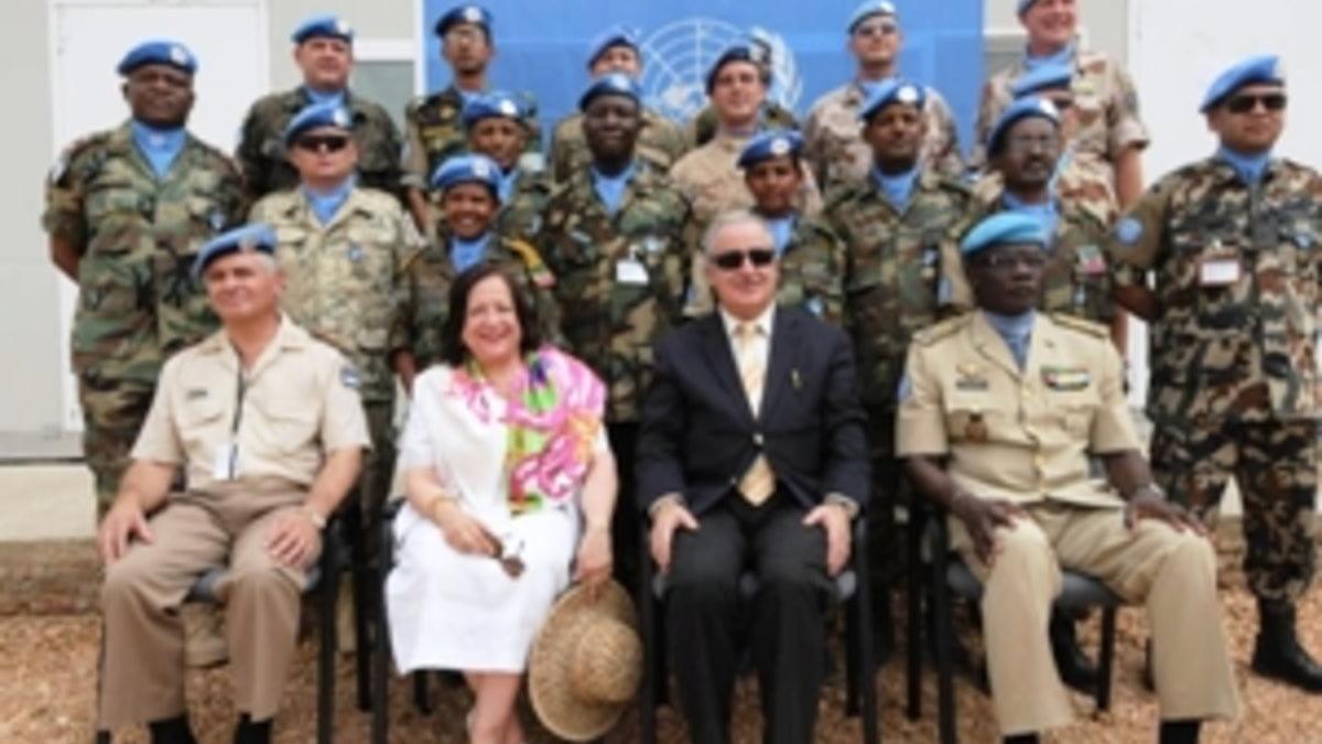 Group photo of peacekeeping personnel in military uniforms and blue berets, seated and standing in rows in front of a UN backdrop.