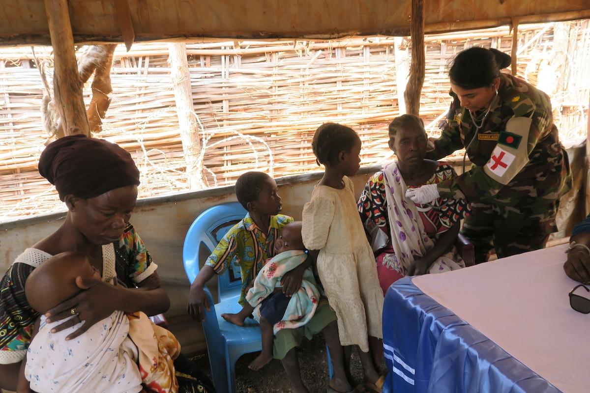 More than 400 internally displaced persons in Wau were keen to get free medical check-ups when Bangladeshi peacekeepers visited their camp. Photos: Jimmy Lambs Ludanga/UNMISS A uniformed medical officer is providing treatment to a seated woman. Next to the female patient is another woman and three children.